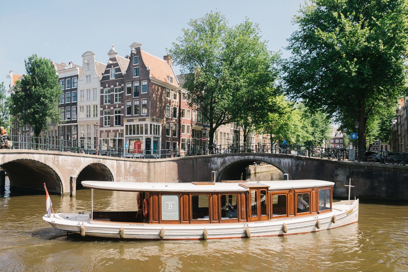Klassieke salonboot vaart onder een brug door een Amsterdamse gracht