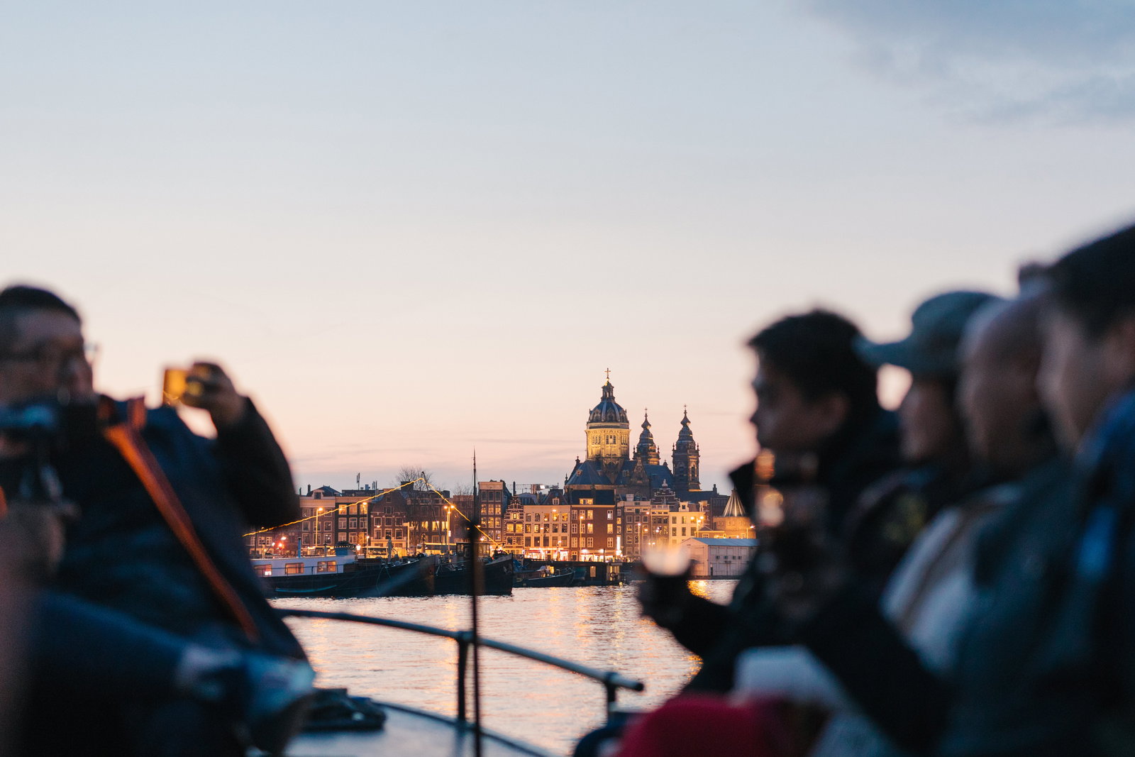 Gasten aan dek met de verlichte Amsterdamse skyline in de avond